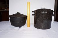 Side view showing footed cast iron cauldron on left next to vented double boiler on right, with ruler for size reference.