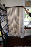 Full view of wooden beaded doorway curtain hanging between two shelves with DVDs.