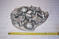 Top-down view of Nordic Ware Backyard Bugs bake pan showing insect shapes with measuring tape for scale (about 12 inches wide).