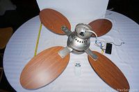 Photo showing the entire ceiling fan assembly with four wooden blades attached to the motor housing and the remote placed below.