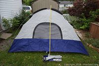 Fully assembled Escort UV-Tex 5 dome tent with fly cover shown upright outside on grass with carry bag and yellow measuring stick in front.