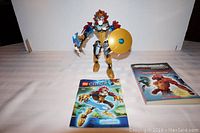 Photo showing Lego Chima Chi Laval figure with shield and weapon, original instructions booklet, and Bionicle book.