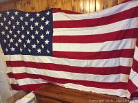 Full view of vintage American flag hanging against wooden wall, showing all stripes and stars.