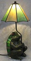 Front view of the figural frog lamp lit with stained glass shade