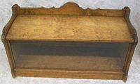 View of the solid maple wood cabinet from the front with the glass panel closed, showing the wood grain and decorative top edge.