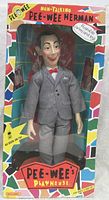 Front view of Pee-Wee Herman doll in original box showing doll dressed in gray suit with red bowtie.