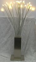 Front view of IKEA STRANNE Medusa Tree LED table lamp lit with warm LED bulbs, showing curved clear acrylic stems and brushed steel base.