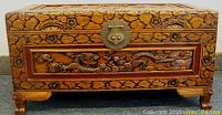 Front view of carved wood jewelry chest with floral and dragon patterns, metal clasp lock present, showing some wear and scuff marks.