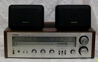 Front view of Technics by Panasonic FM/AM stereo receiver with two Aiwa speakers on top, showing wood sides and silver front panel with branded logos and controls.