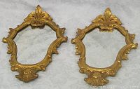 Pair of gilt framed ornate wood hall mirrors shown side by side on fabric background, showing full frame and mirror shape.