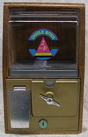 Front view showing clear plastic dispenser compartment with colorful label and metal coin mechanism with lever and handle.