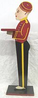 Side profile view of the wooden figure showing the painted details of the bellhop's face, uniform, and tray.