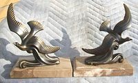 Pair of bronzed bird bookends on rectangular tan marble bases, viewed in full.
