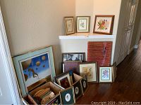 Overview of many framed pieces and boxed art prints on floor and ledge showing size and variety.