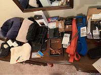 Photo of travel accessories including neck pillow, eye masks, bags, passport holder, map, straps, clocks, and cameras on a surface under a mirror