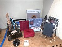 Wide shot of all items on wood table including music box, photo album, glass frame, pens, and jewelry boxes.
