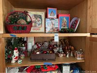 Two shelves filled with assorted Christmas decorations including a basket with pine cones, figurines, ornaments in a tray, and a miniature gingerbread house.