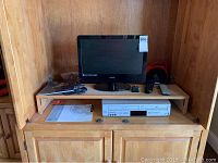 19 inch Vizio flat screen TV, Panasonic VHS DVD combo, remotes, ear buds, and extension cord placed inside wooden cabinet.