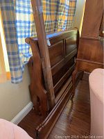 Disassembled queen size sleigh bed frame components including the headboard with classic curved sleigh shape, medium brown wood finish, and wooden panels.