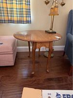 Drop leaf end table shown with one leaf dropped down, oval top shape, carved wood detailing on apron, Queen Anne style legs with ball and claw feet, some surface scratches and discoloration visible
