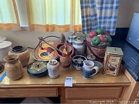 Table with various ceramic and metal canisters, bowls, cookie jar, and basket of artificial apples.