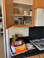 Kitchen cabinet with measuring cups, metal cookie cutters, salt and pepper shakers and crocheted kitchen cloths on the counter below.