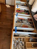 Kitchen drawer with various utensils including whisks, can opener, scissors, and wine openers organized in compartments.