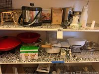 Full lot view showing a variety of kitchen items arranged on shelves including a wok, colanders, food masher, cream whipper, multi slicer, ice bucket, and various kitchen tools.