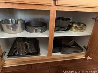Cabinet shelf containing multiple baking pans, tins, and cookie sheets.