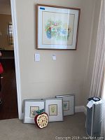 The lot of ten pieces of framed wall art and the Apple wall clock placed on the floor leaning against the wall. Various sizes and frame colors are visible including wood and metal frames.