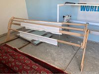 Wide angled photo of the entire wooden quilting frame with fabric bars mounted, showing one side and base support on concrete floor