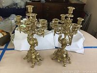 Pair of brass candelabra displayed side by side on table with background items visible