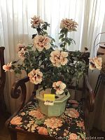 Asian jade plant with pink and white flowers arranged in a green hexagonal ceramic planter, placed on a floral upholstered chair.