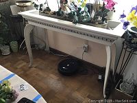 Full view of white painted wooden plant stand with plants on top, showing curved legs and visible wear on paint.