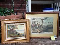 Two framed artworks displayed side-by-side outdoors against brick background; one smaller oil painting with a wooden frame, one larger hunting print in a wooden frame.