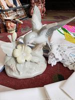 Ceramic bird figurine with butterfly and flower detail, white and gray colors, placed on embroidered linens