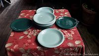 Overview showing six light green plates stacked and arranged with six dark green plates on a red floral tablecloth.