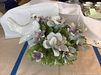 Porcelain basket with white bird and multi-colored porcelain flowers and leaves, viewed from the front and side angles.