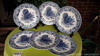 Six blue and white decorative Thanksgiving plates displayed on stands and laid flat, showing the turkey design and floral patterned border.
