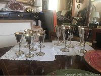 Wide angle photo showing all 12 silver plate goblets, arranged in two groups of six on white cloth.
