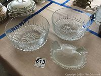 Two large crystal bowls with detailed design and a clear glass hen candy dish on a beige tablecloth.