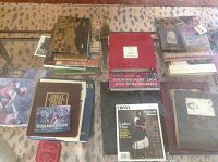 Overhead photo showing multiple coffee table hardcover books stacked on a glass coffee table with patterned carpet underneath. Titles and covers visible include Ebony magazine with Michelle Obama, Great Crafts of the World, and others.