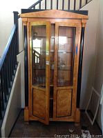 Full front view of tall wood curio cabinet with two glass doors and black decorative columns. Cabinet doors partially open showing glassware inside.