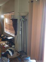 Floor lamp standing next to wall and curtain in a living area, showing full height and setting.