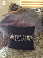 Photo showing ostrich feather throw blanket and black pillow placed on a patterned couch with the throw folded behind the pillow.