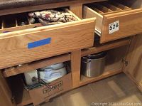 Wooden kitchen cabinet drawers showing a cardboard box with ceramic and metal pots and a metal pot.