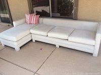 Full view of cream colored outdoor sectional sofa with chaise showing overall form and color, including two pillows.