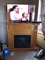 Front view of wooden electric fireplace with electric firebox and TV on top.
