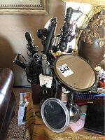 Photo showing two metal-framed table mirrors and a container holding multiple black handled curling irons and hair straighteners