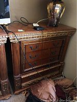 Front view of the wooden dresser, showing three drawers with metal handles, decorative carved moulding on the top and sides, and minor surface wear.